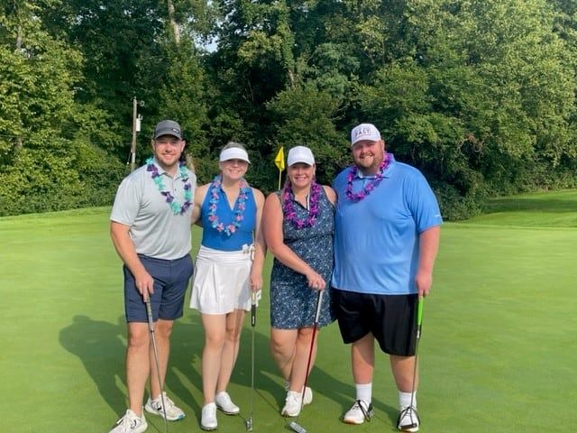 Four golfers wearing colorful leis posing together on golf course green
