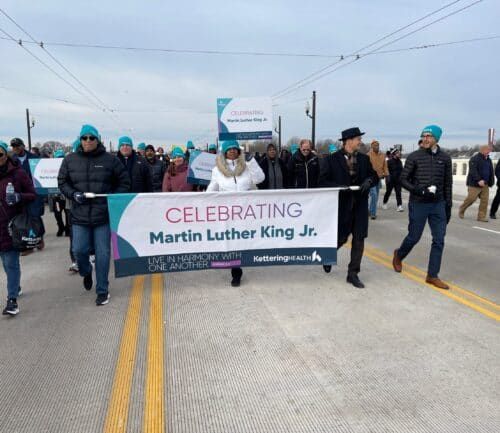Group marching across bridge carrying "Celebrating Martin Luther King Jr." banner during commemorative event.