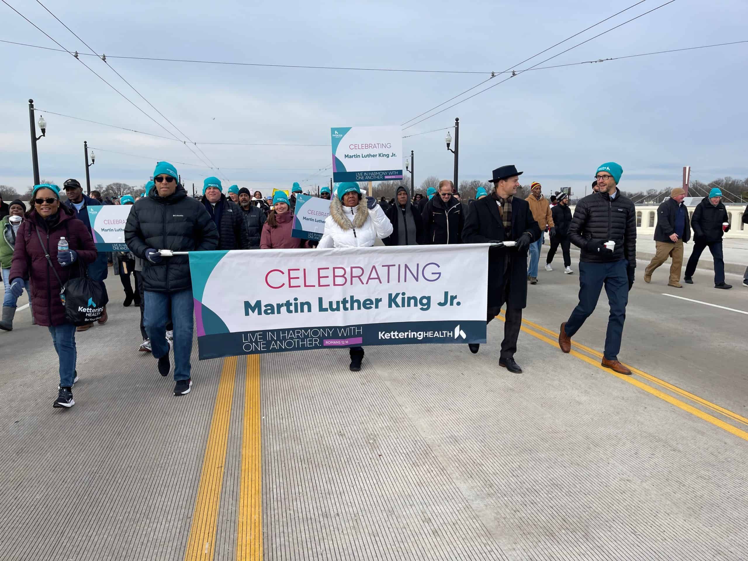 Group marching across bridge carrying "Celebrating Martin Luther King Jr." banner during commemorative event.