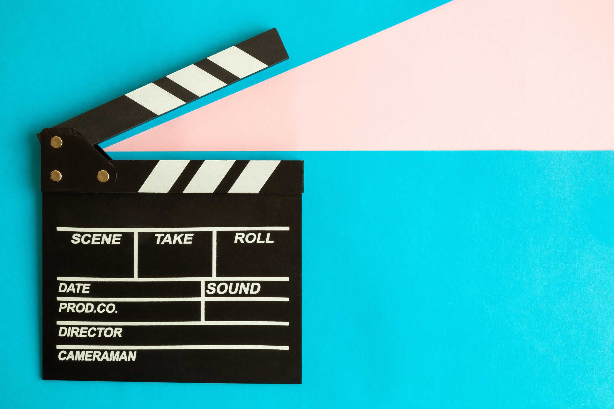Black film clapperboard with white diagonal stripes on bright blue and pink background.