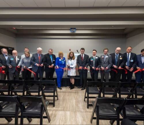 Group of officials holding scissors at red ribbon cutting ceremony in conference room