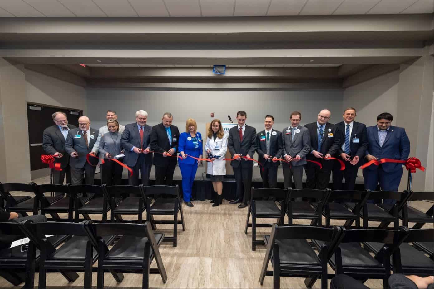 Group of officials holding scissors at red ribbon cutting ceremony in conference room