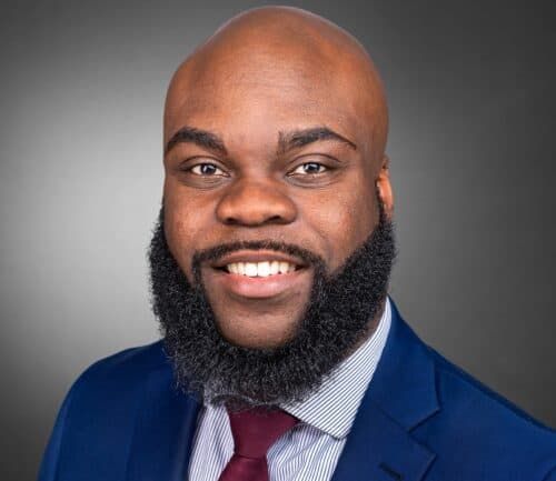 Professional headshot of Norm Spence in navy suit with burgundy tie smiling
