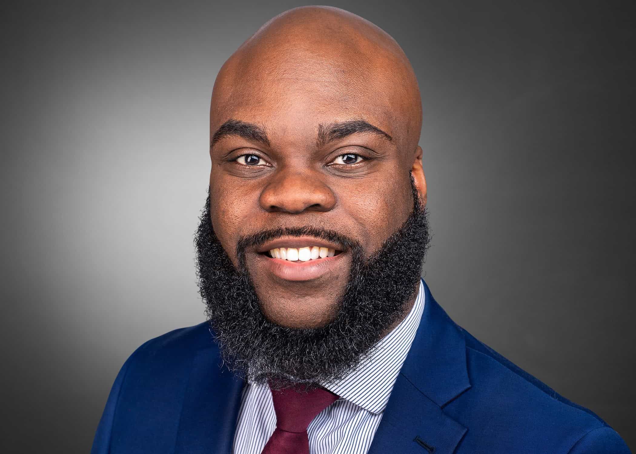 Professional headshot of Norm Spence in navy suit with burgundy tie smiling