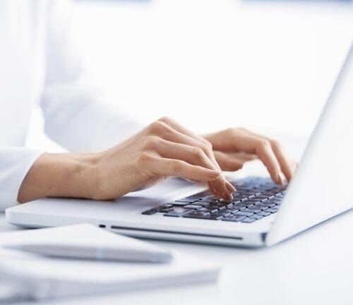 Hands typing on white laptop keyboard at modern office desk