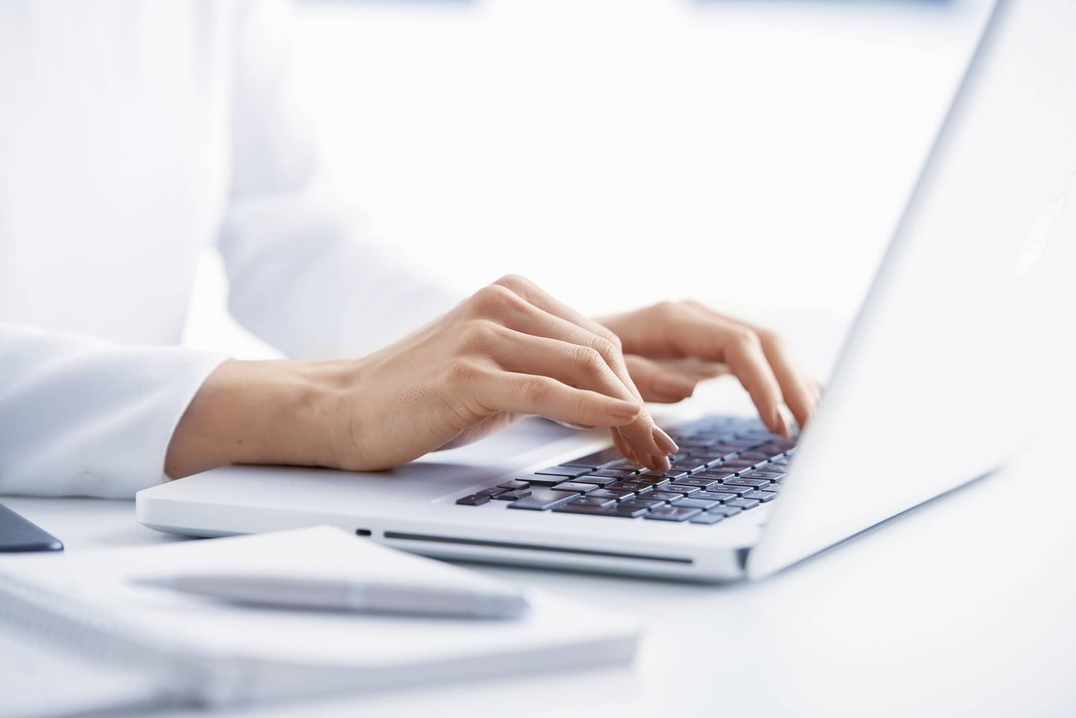 Hands typing on white laptop keyboard at modern office desk