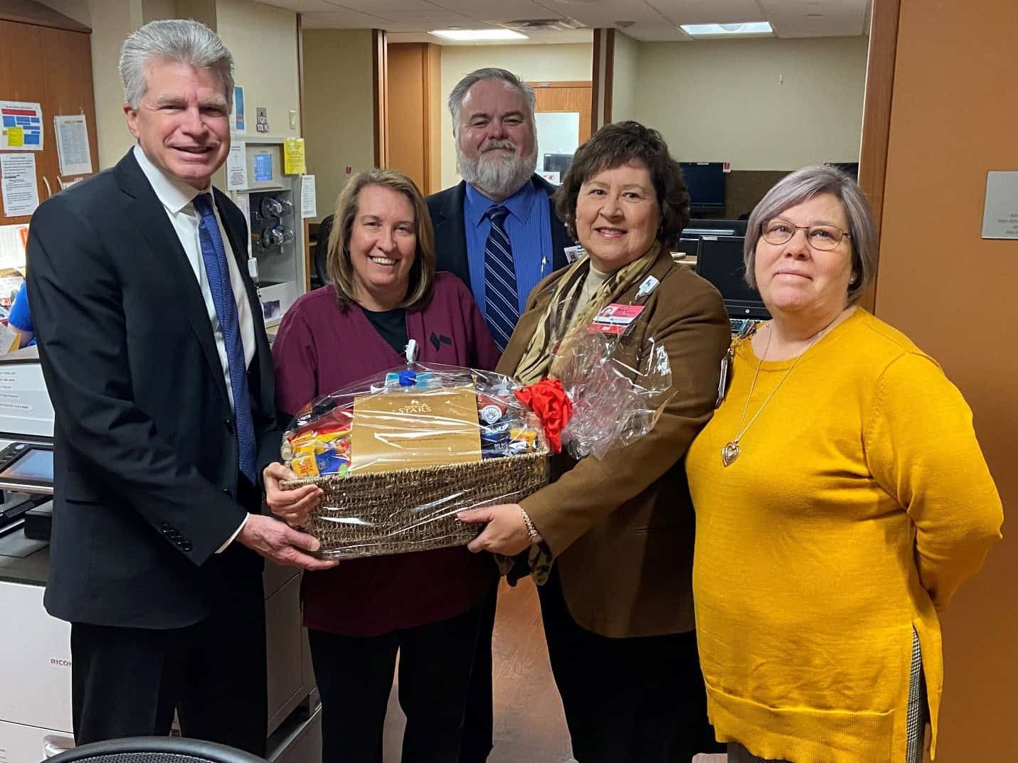 Five healthcare professionals presenting gift basket to employee recognition recipient
