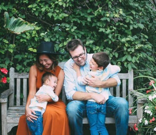 Happy family of four sitting together on garden bench surrounded by flowers