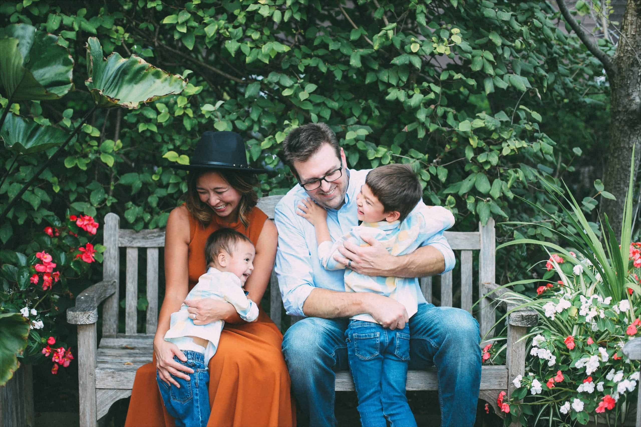 Happy family of four sitting together on garden bench surrounded by flowers