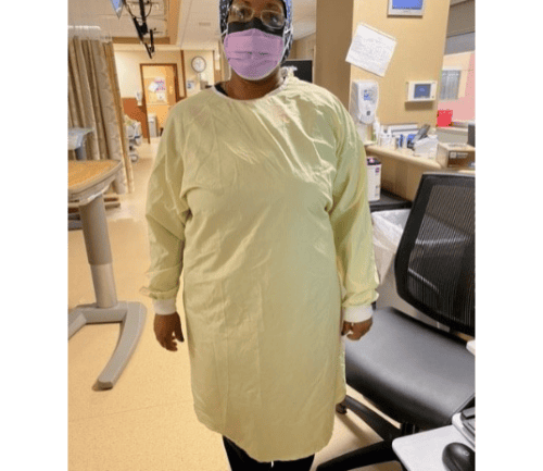 Healthcare worker in yellow protective gown and mask standing in hospital room