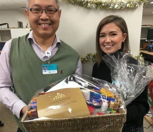 Two healthcare employees holding gift basket with Constellation Award certificate and holiday decorations