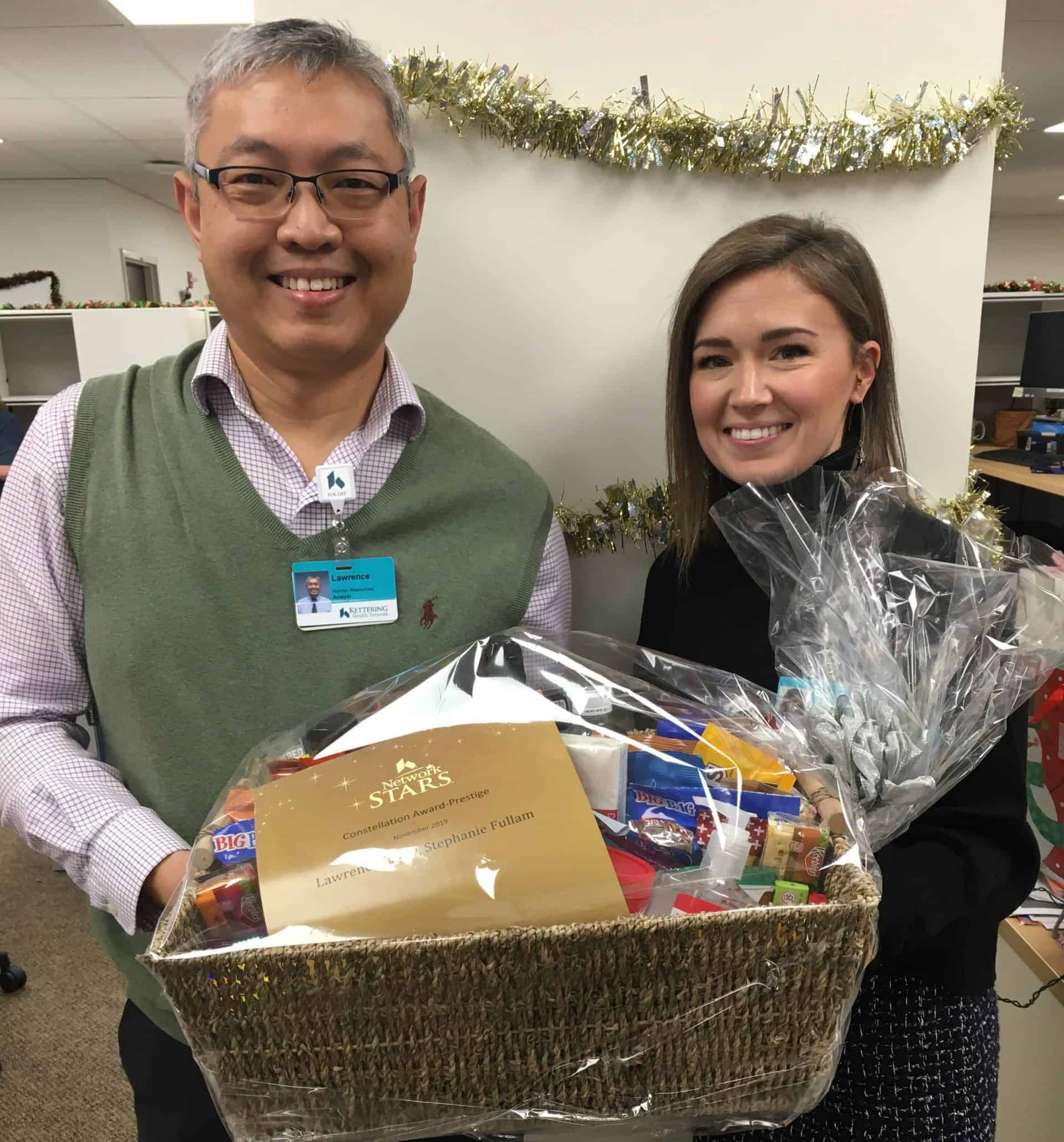 Two healthcare employees holding gift basket with Constellation Award certificate and holiday decorations