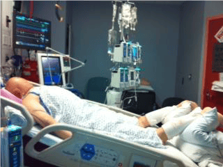 Patient lying prone in hospital bed surrounded by medical equipment and monitors