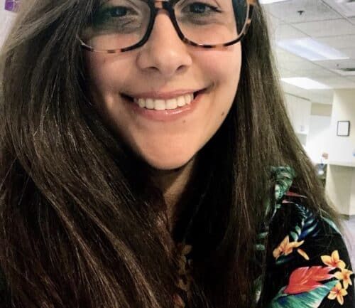 Professional headshot of Roberta Vieira de Oliveira wearing glasses and tropical print top