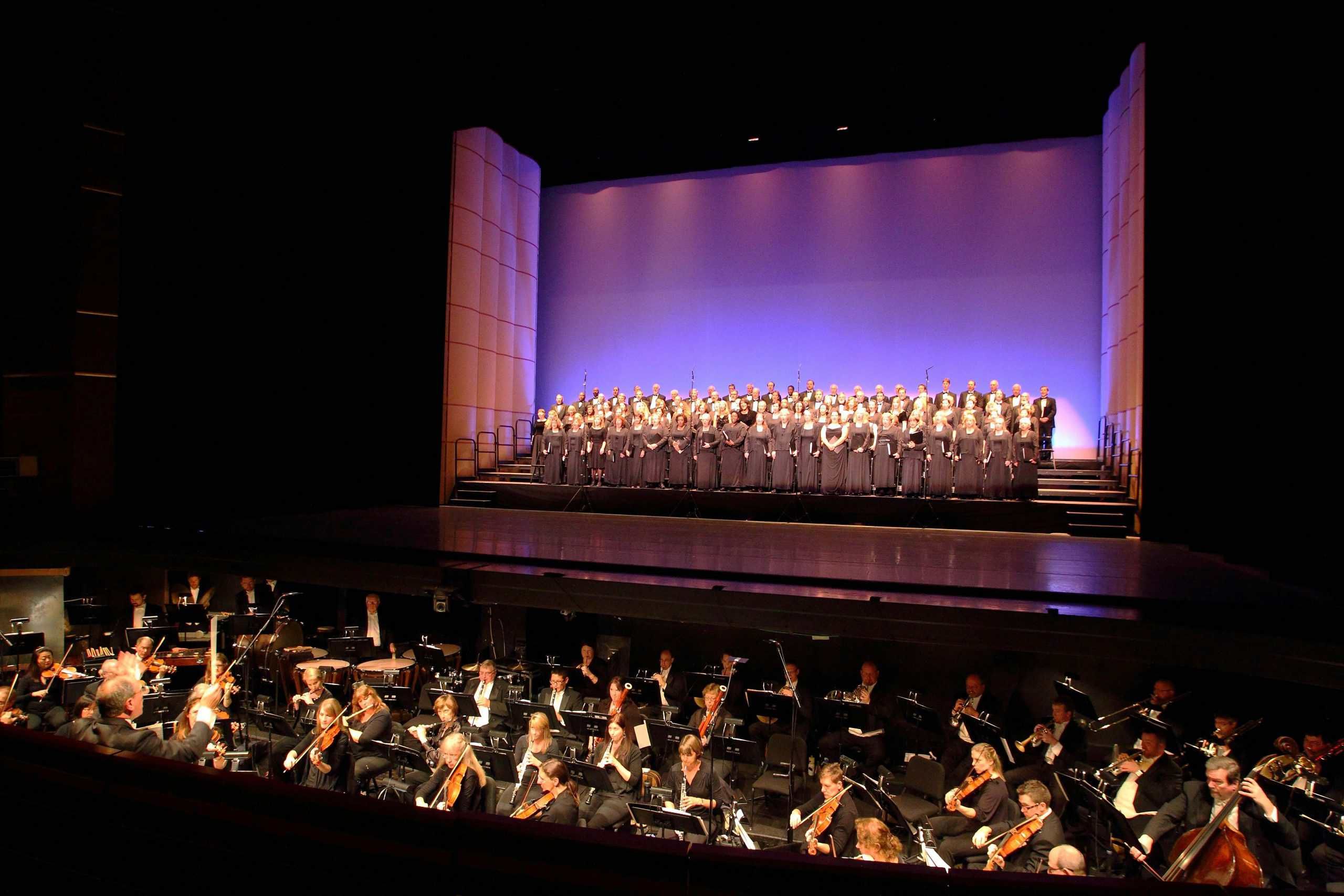 Large choir performing on stage with orchestra in concert hall setting