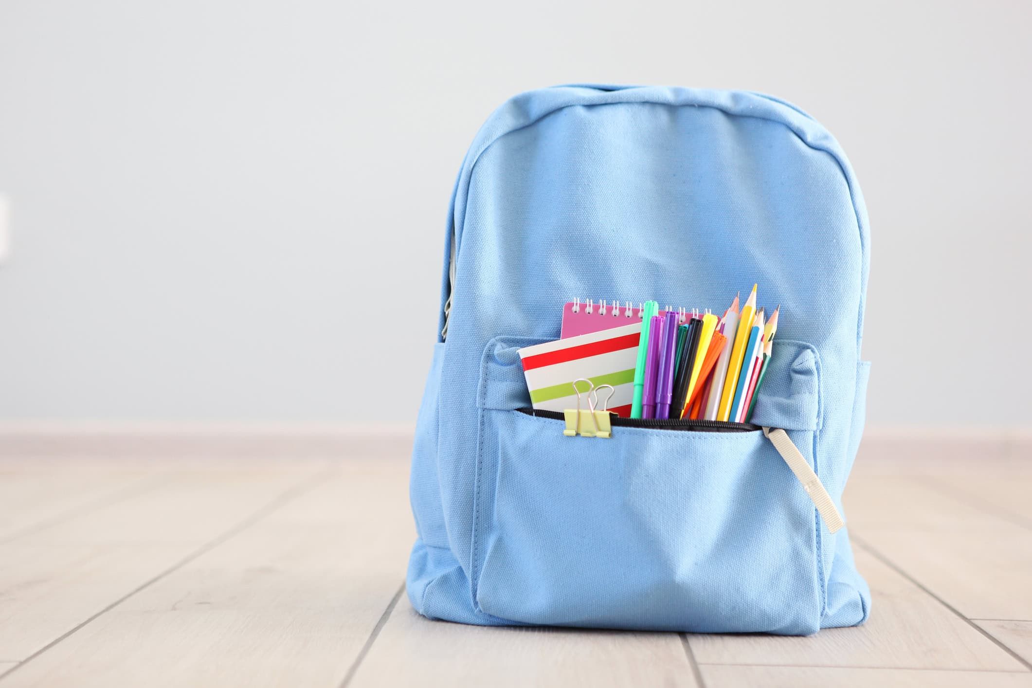 Blue school backpack filled with colorful pencils, notebooks and school supplies