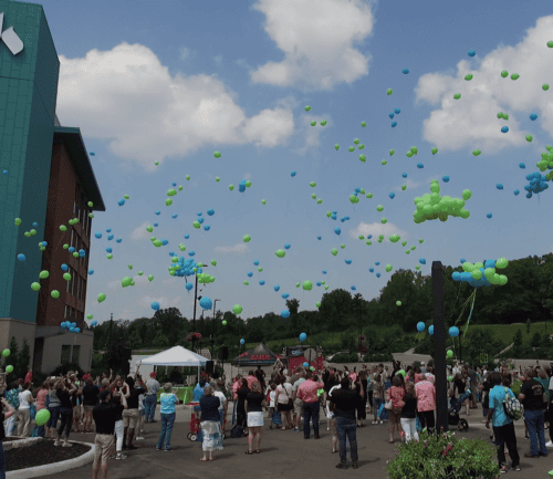 Crowd of people releasing green and blue balloons into sky at healthcare facility celebration
