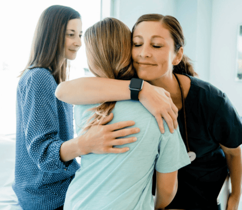 Healthcare provider embracing patient while another provider looks on supportively