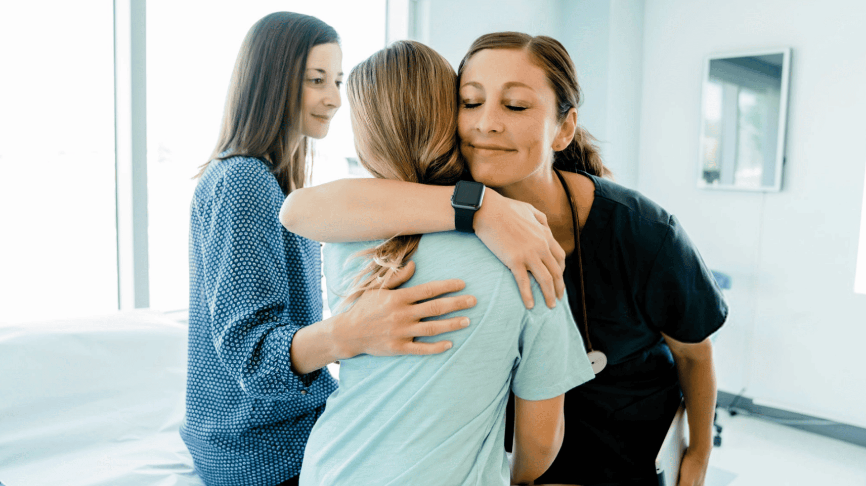 Healthcare provider embracing patient while another provider looks on supportively