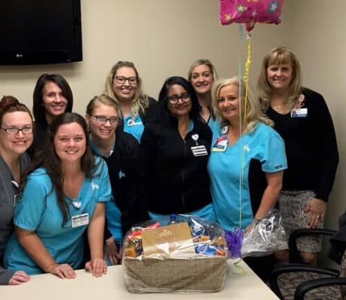 Healthcare team celebrating employee with gift basket and balloon in break room