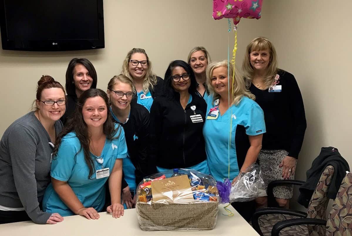 Healthcare team celebrating employee with gift basket and balloon in break room
