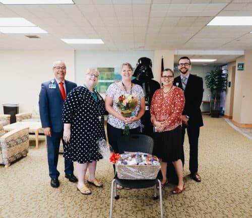 Healthcare staff celebrating with flowers and gift basket in hospital lobby
