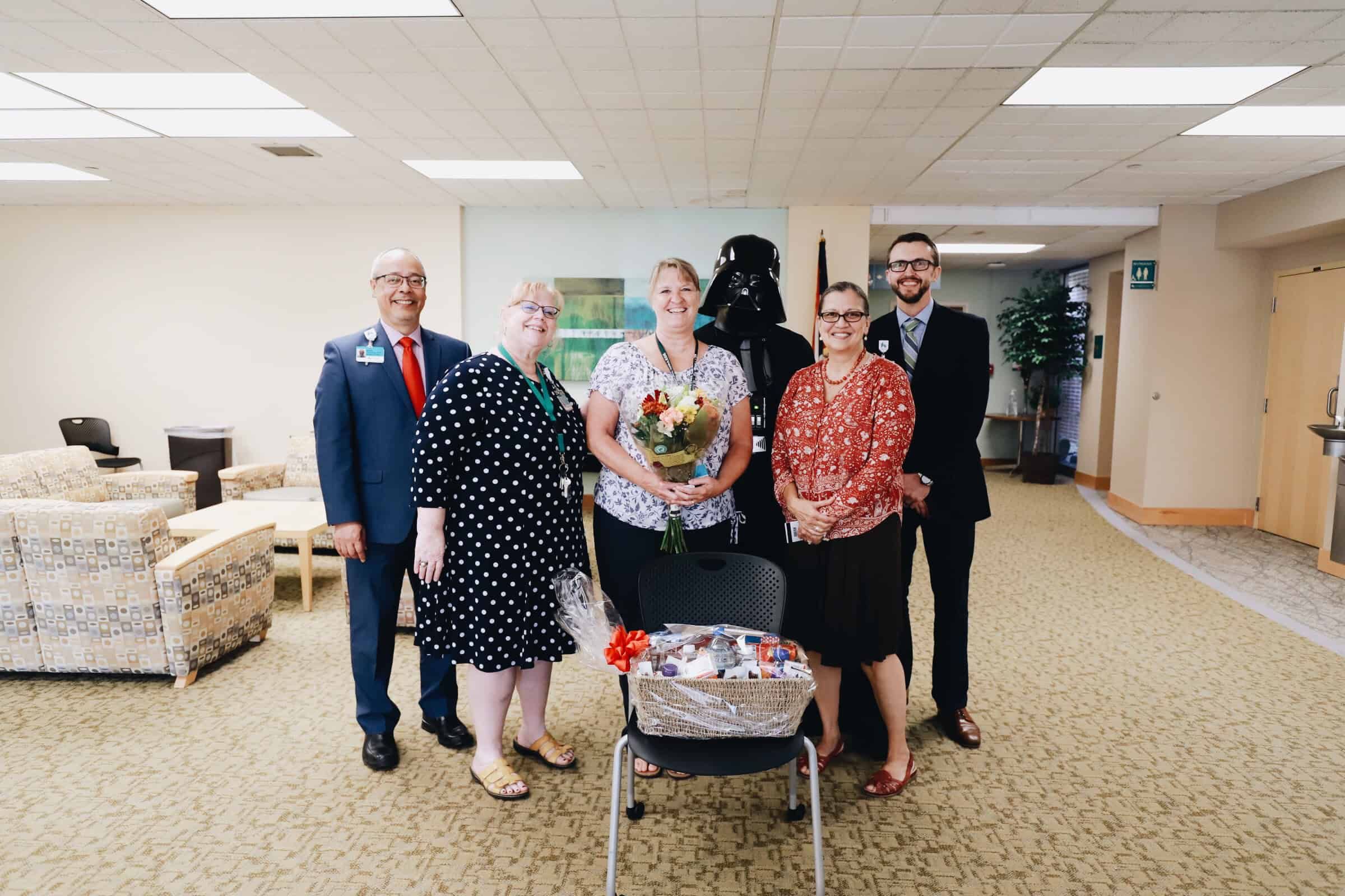 Healthcare staff celebrating with flowers and gift basket in hospital lobby