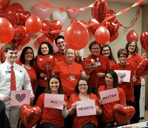 Healthcare team celebrating with red heart balloons holding "All Hearts Matter" signs