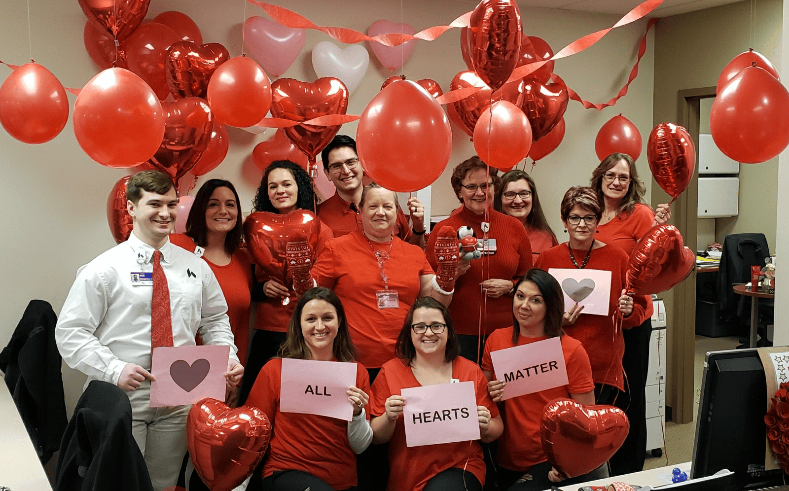 Healthcare team celebrating with red heart balloons holding "All Hearts Matter" signs