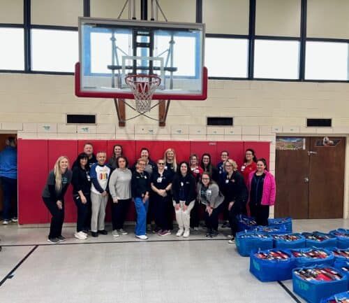 Kettering Health volunteers gathered in school gym with blue donation bags containing shoes