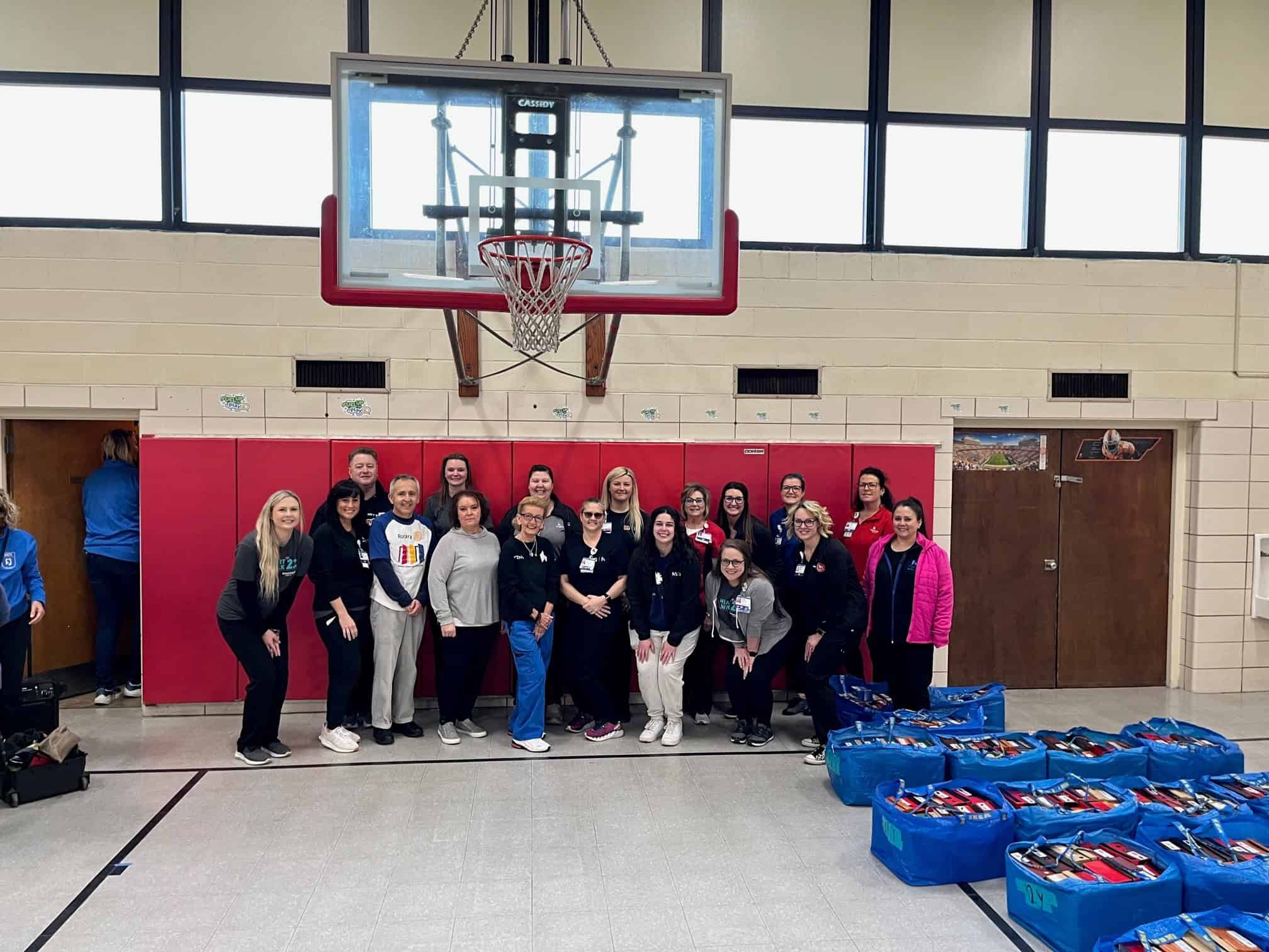 Kettering Health volunteers gathered in school gym with blue donation bags containing shoes