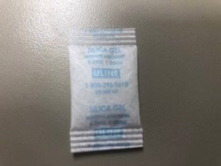 Small white silica gel packet with blue text on textured surface