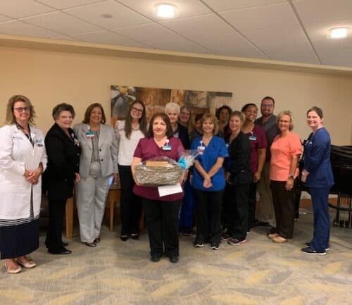 Healthcare team celebrating with Stephanie Austin holding recognition award in hospital break room