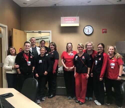 Emergency department staff posing together in hospital hallway wearing scrubs and ID badges