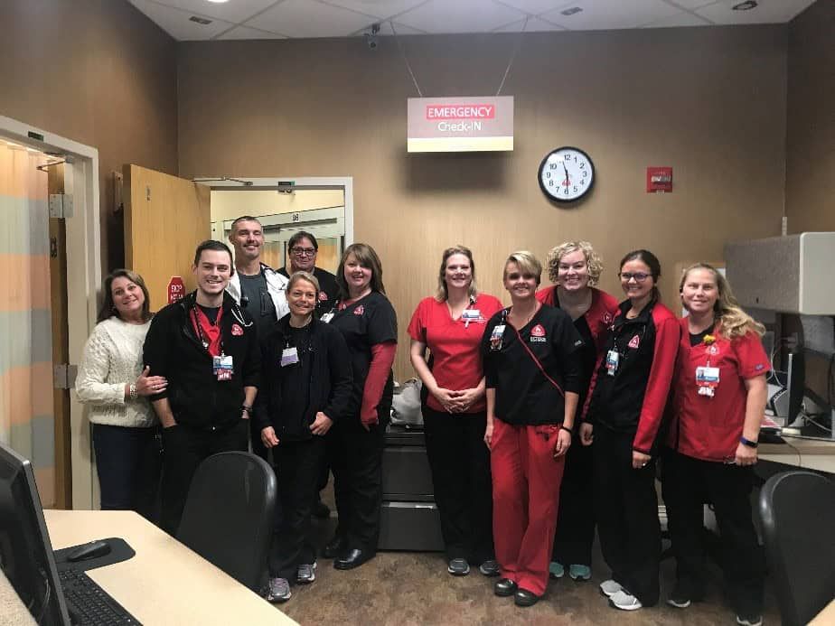 Emergency department staff posing together in hospital hallway wearing scrubs and ID badges