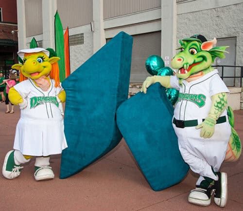 Two Dayton Dragons mascots in white uniforms posing with large blue letters