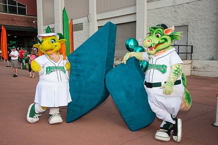 Two Dayton Dragons mascots in white uniforms posing with large blue letters