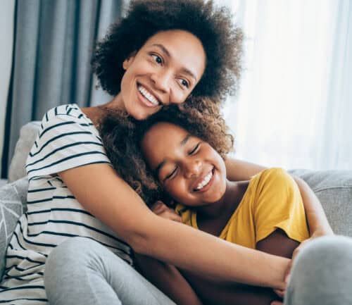 Happy mother hugging her young daughter while sitting together on couch at home