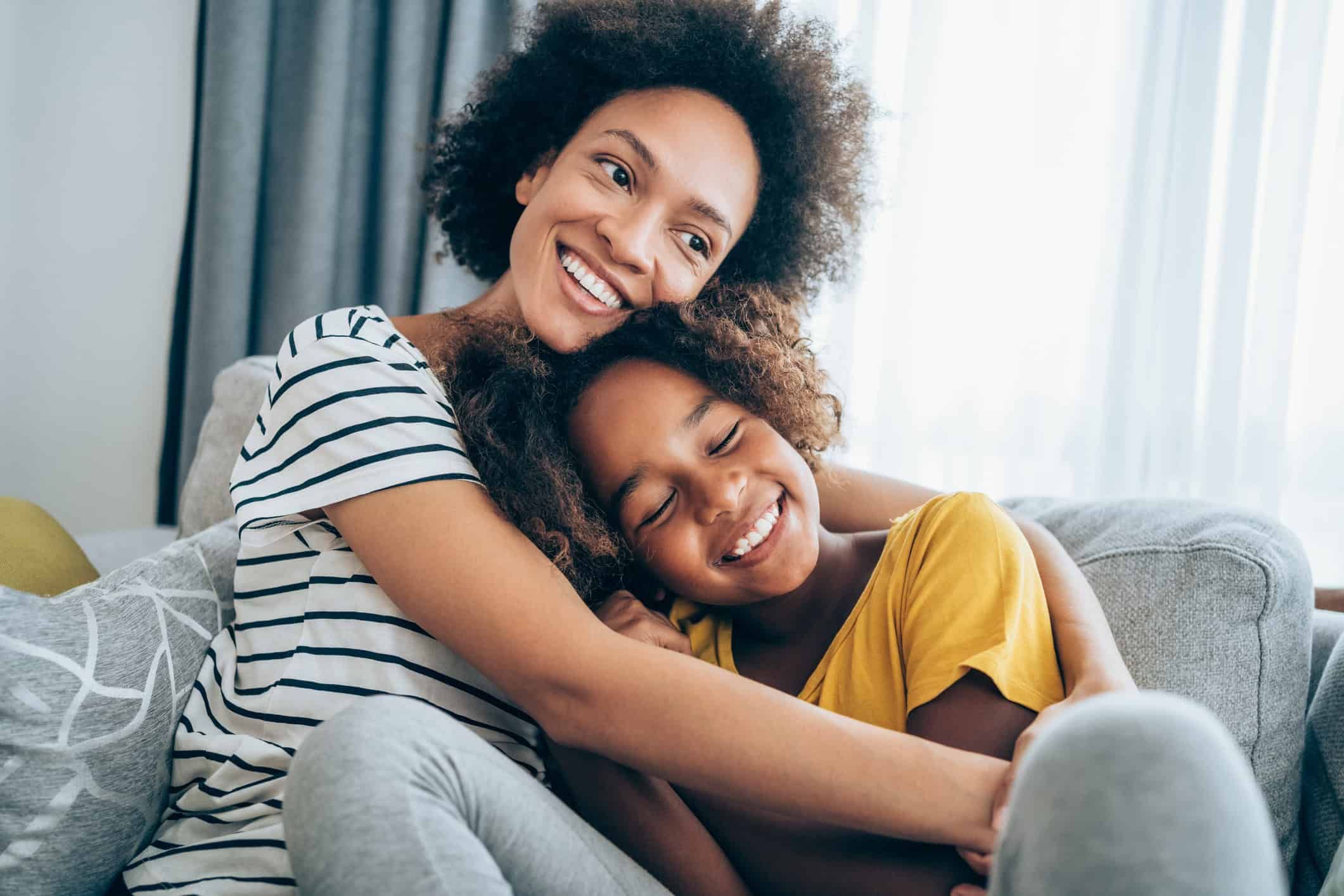 Happy mother hugging her young daughter while sitting together on couch at home