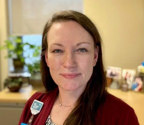 Professional headshot of healthcare worker in burgundy cardigan wearing ID badge