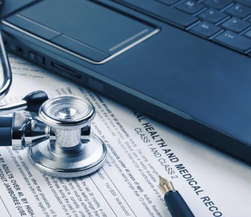 Stethoscope on medical records next to laptop computer on desk