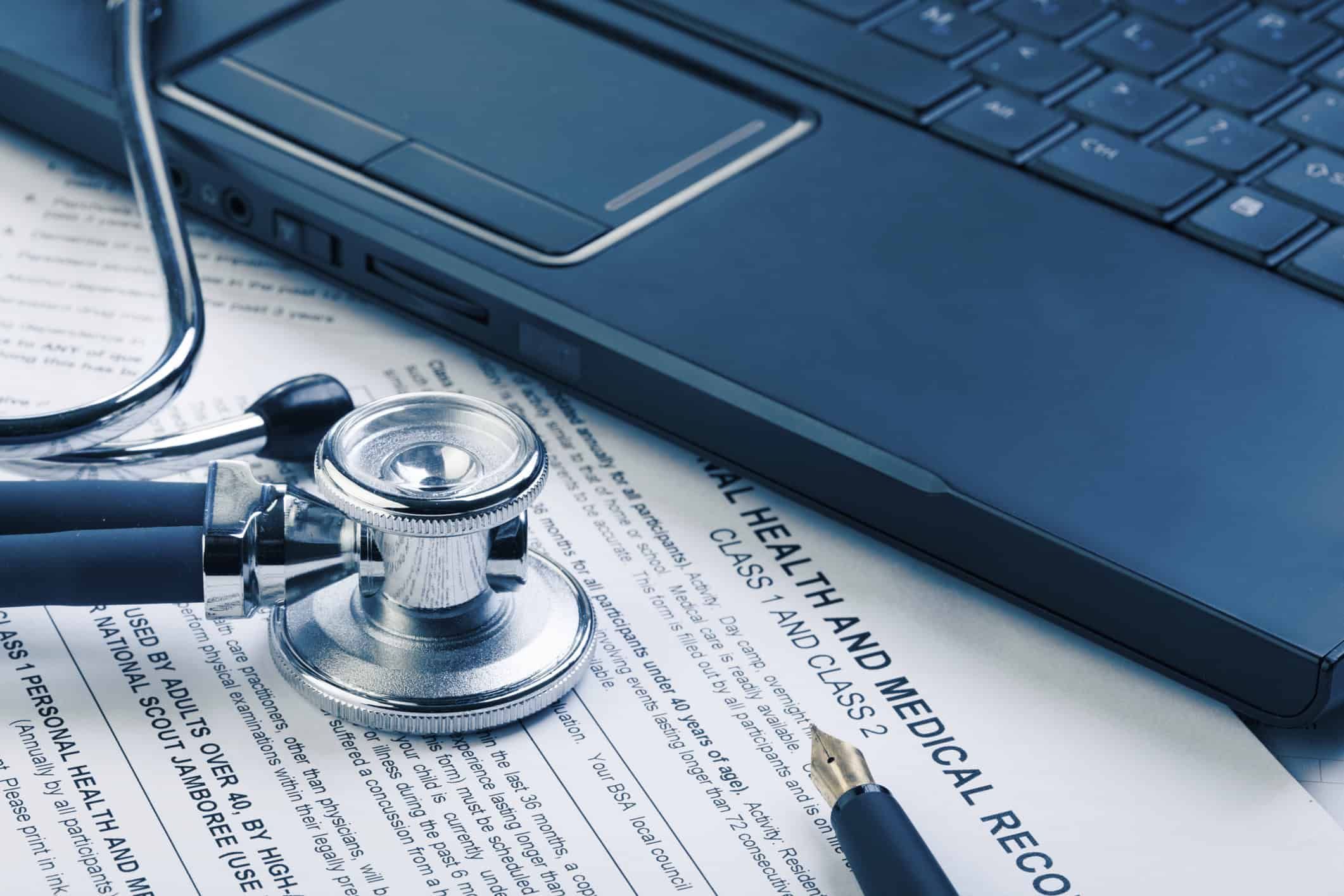 Stethoscope on medical records next to laptop computer on desk