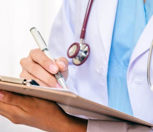 Doctor in white coat with stethoscope writing notes on clipboard
