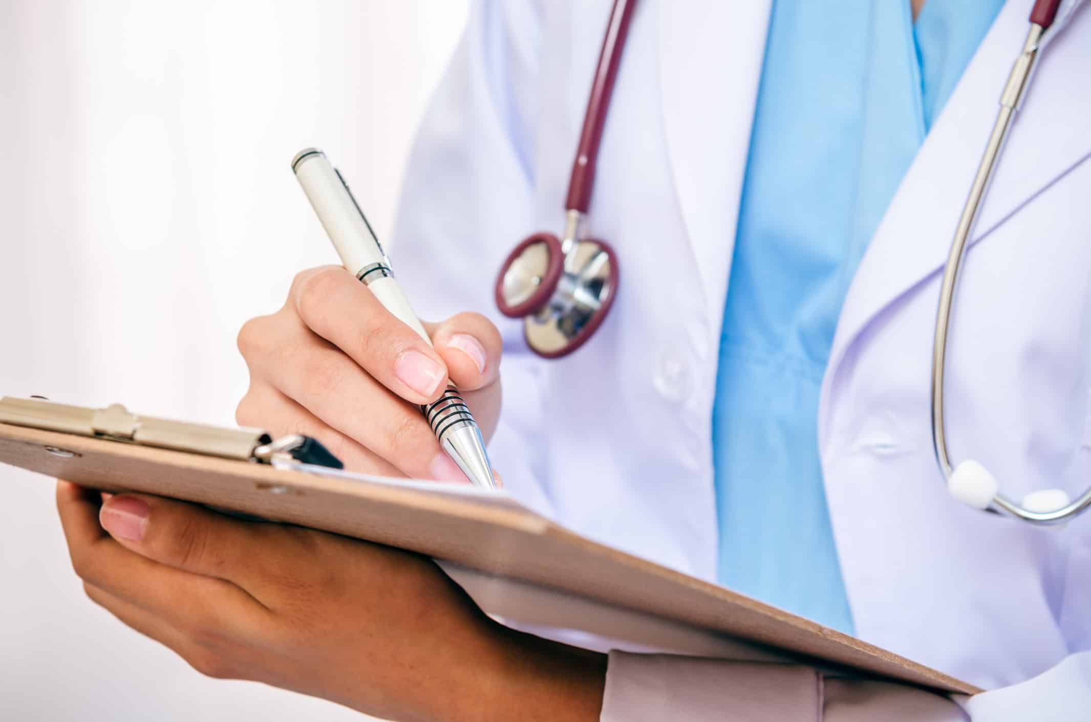 Doctor in white coat with stethoscope writing notes on clipboard