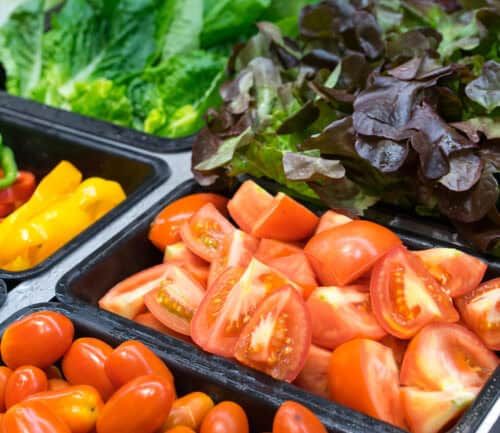 Fresh vegetables including sliced tomatoes, lettuce, and bell peppers arranged in black serving trays