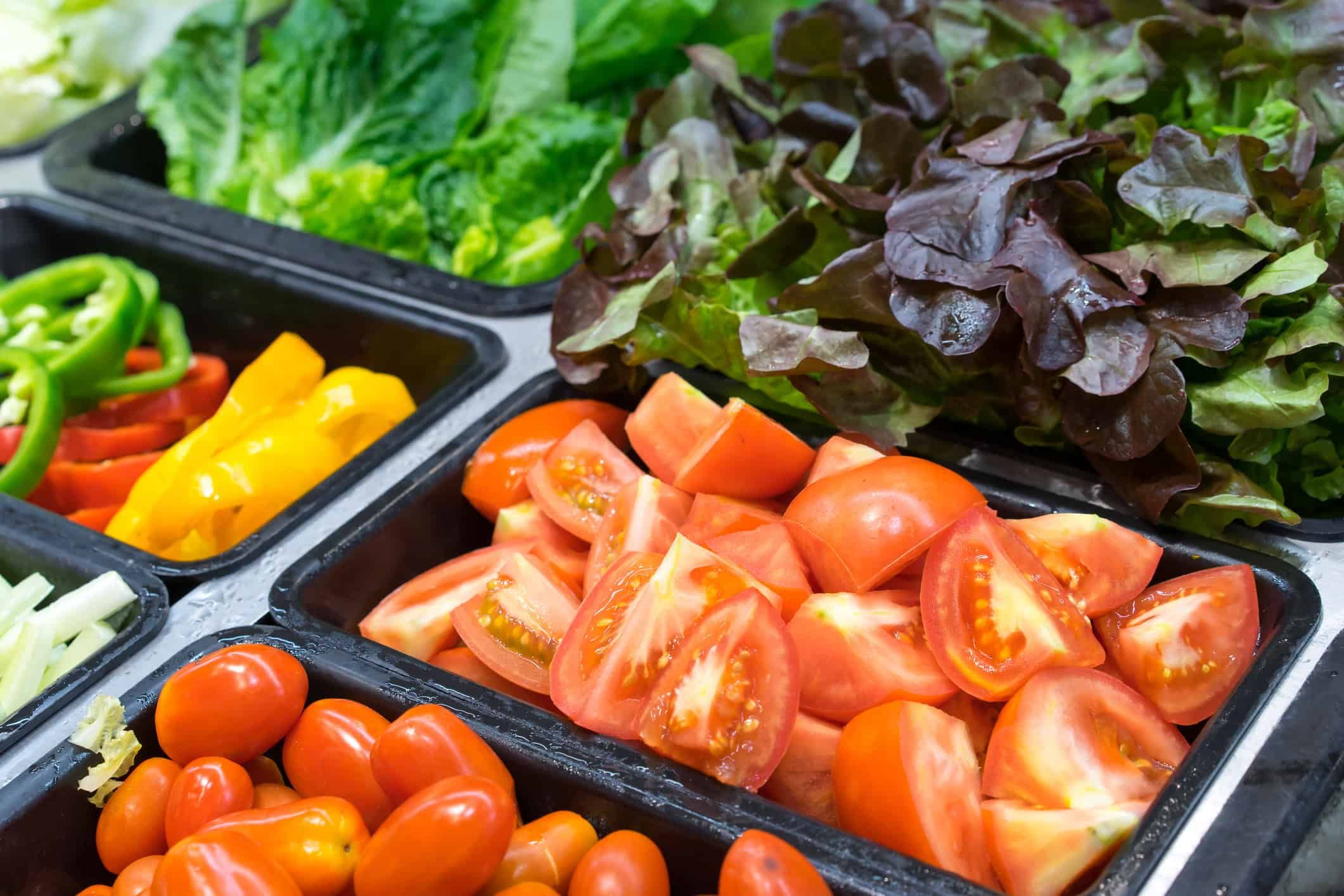 Fresh vegetables including sliced tomatoes, lettuce, and bell peppers arranged in black serving trays