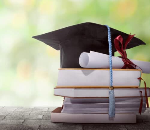 Graduation cap and diploma resting on stack of books outdoors