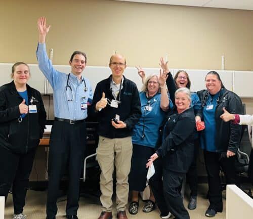 Healthcare team celebrating with raised hands and thumbs up in hospital setting