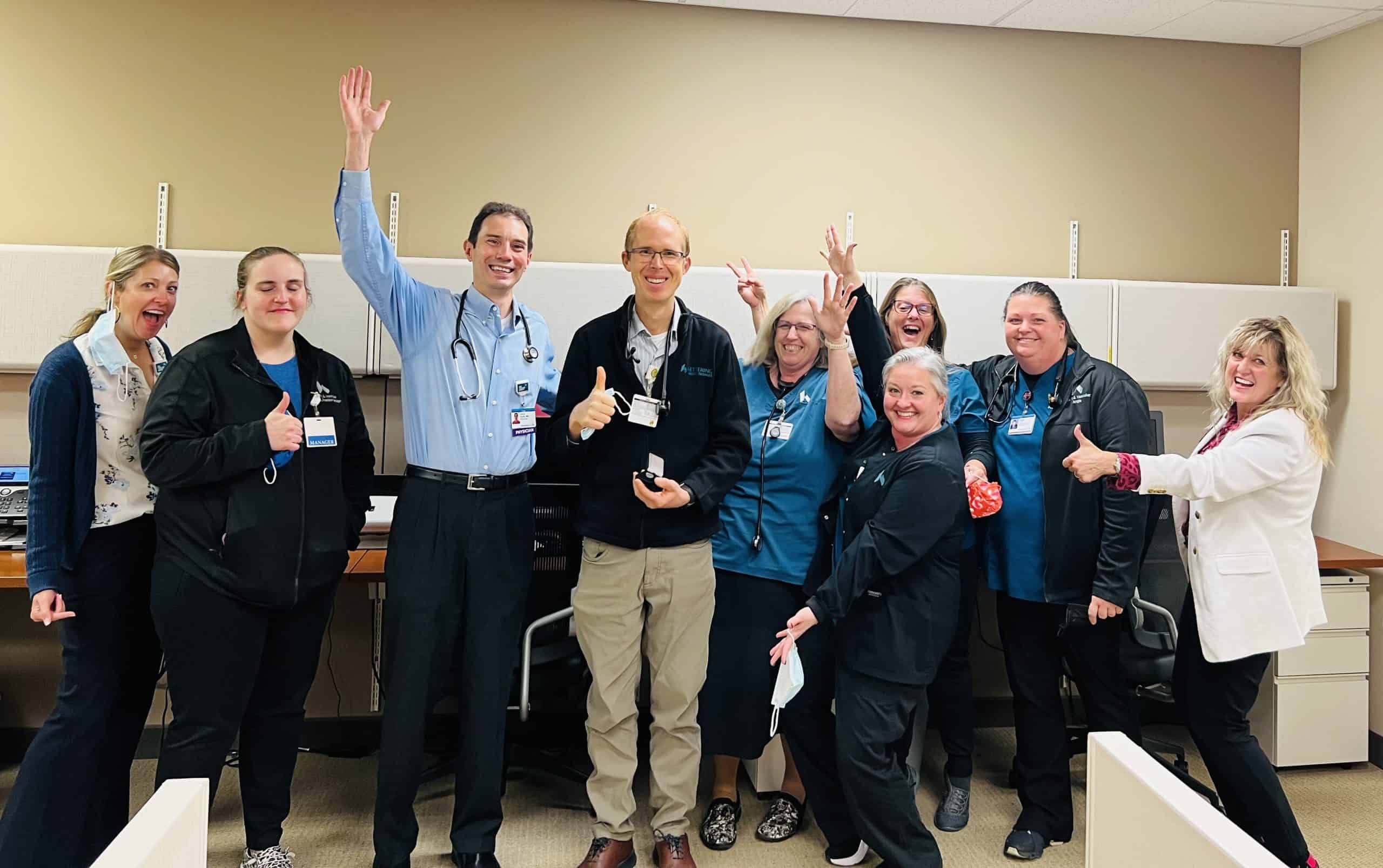 Healthcare team celebrating with raised hands and thumbs up in hospital setting