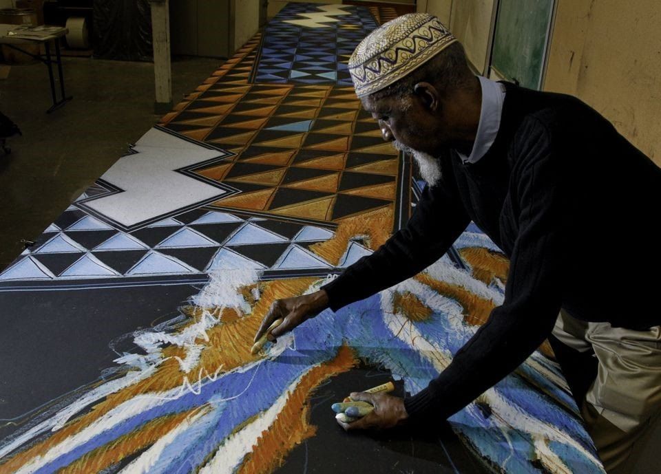 Elderly man in traditional cap painting colorful geometric artwork on large canvas